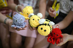 Handmade crochet toys held by people, including a blue octopus, yellow bee, and red octopus.