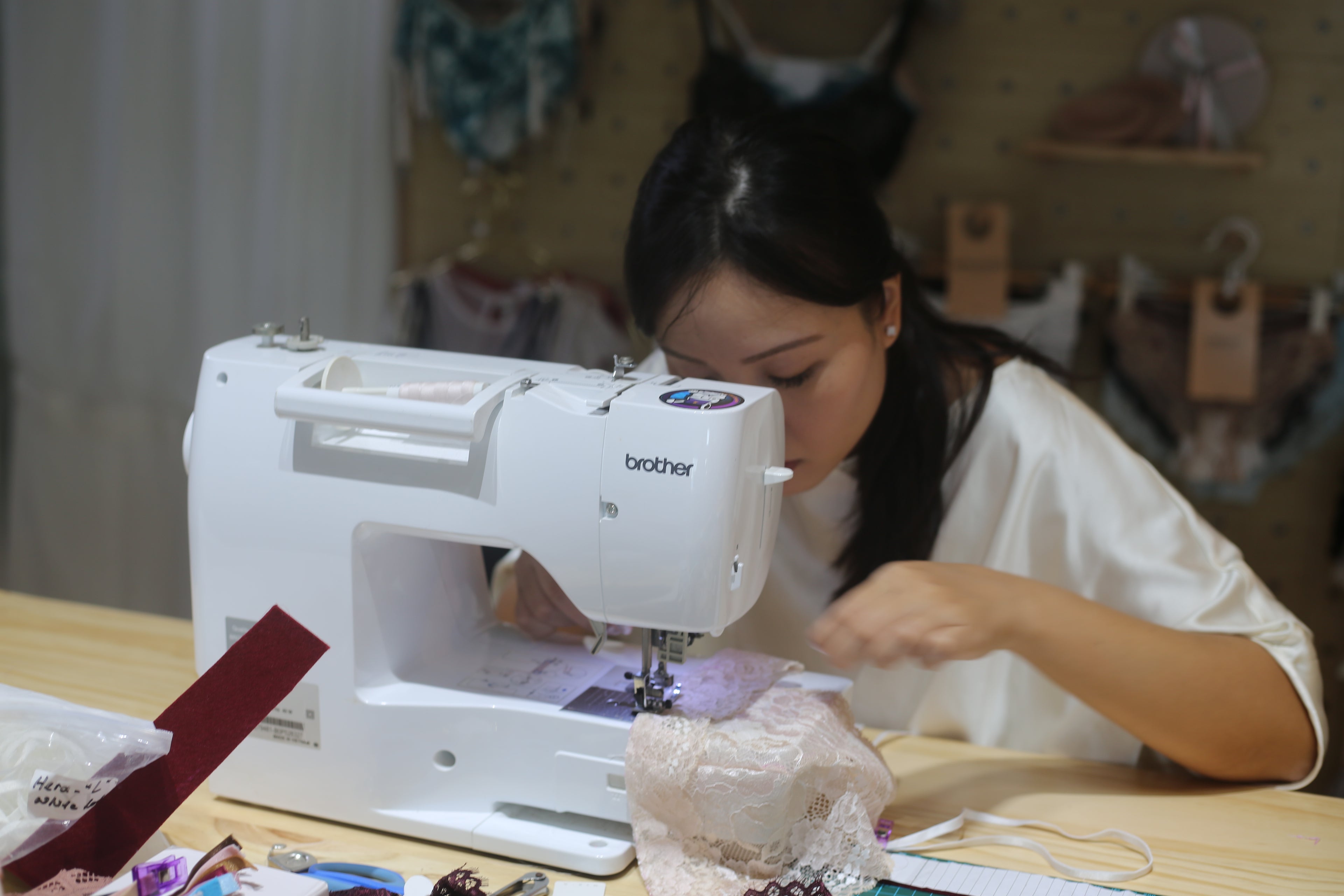 Close-up of a designer threading a specialized sewing machine for lingerie construction with high-quality matching thread.
