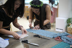 Hand tracing a professional bralette pattern onto delicate lace fabric using a silver fabric marker in a bright design studio.