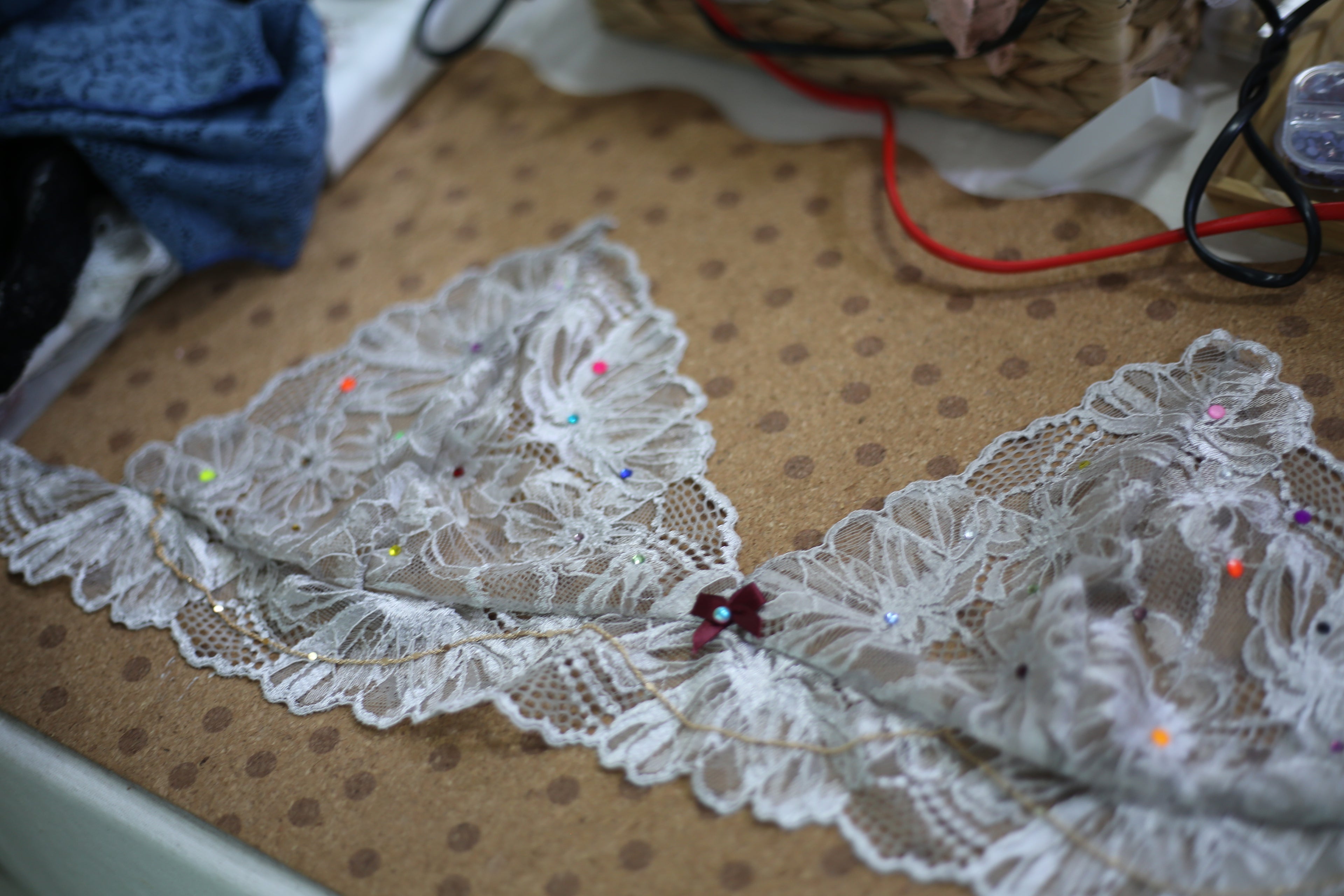 A creator using precision tools to apply shimmering crystals to a lace bralette, adding a touch of bespoke sparkle.